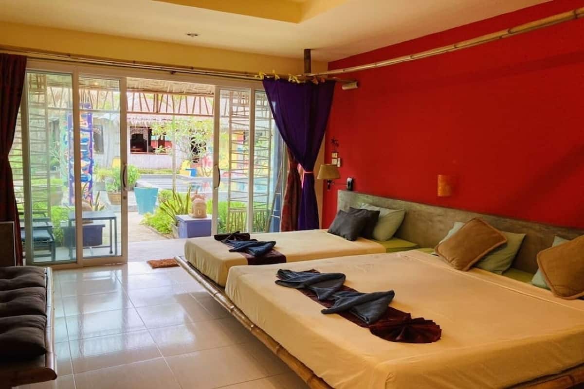 A hotel room with two beds, a red wall, and a sliding glass door leading to an outdoor area with a pool and chairs.
