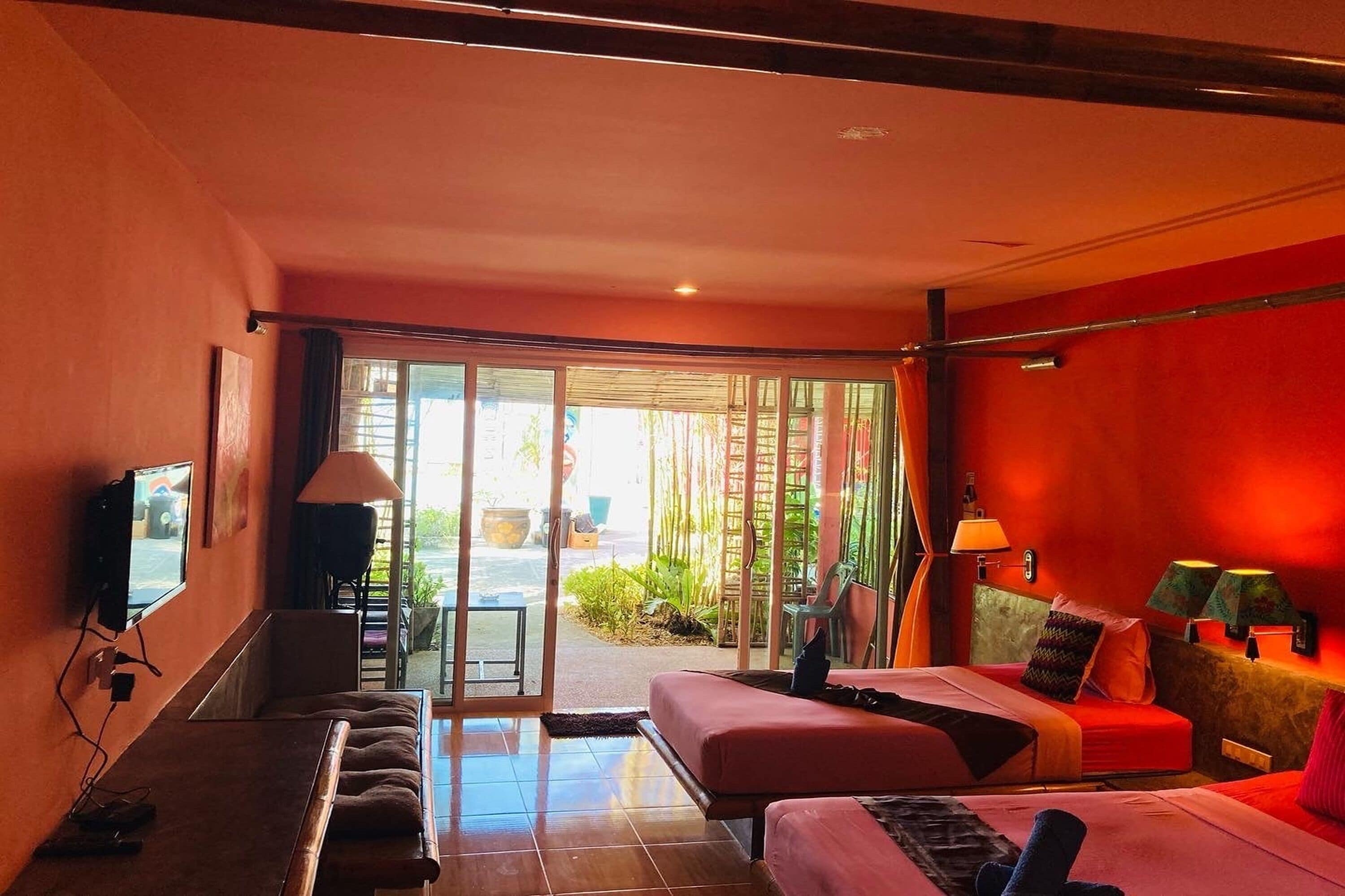A hotel room with a sofa, two beds, a TV, and a sliding glass door leading to an outdoor area.