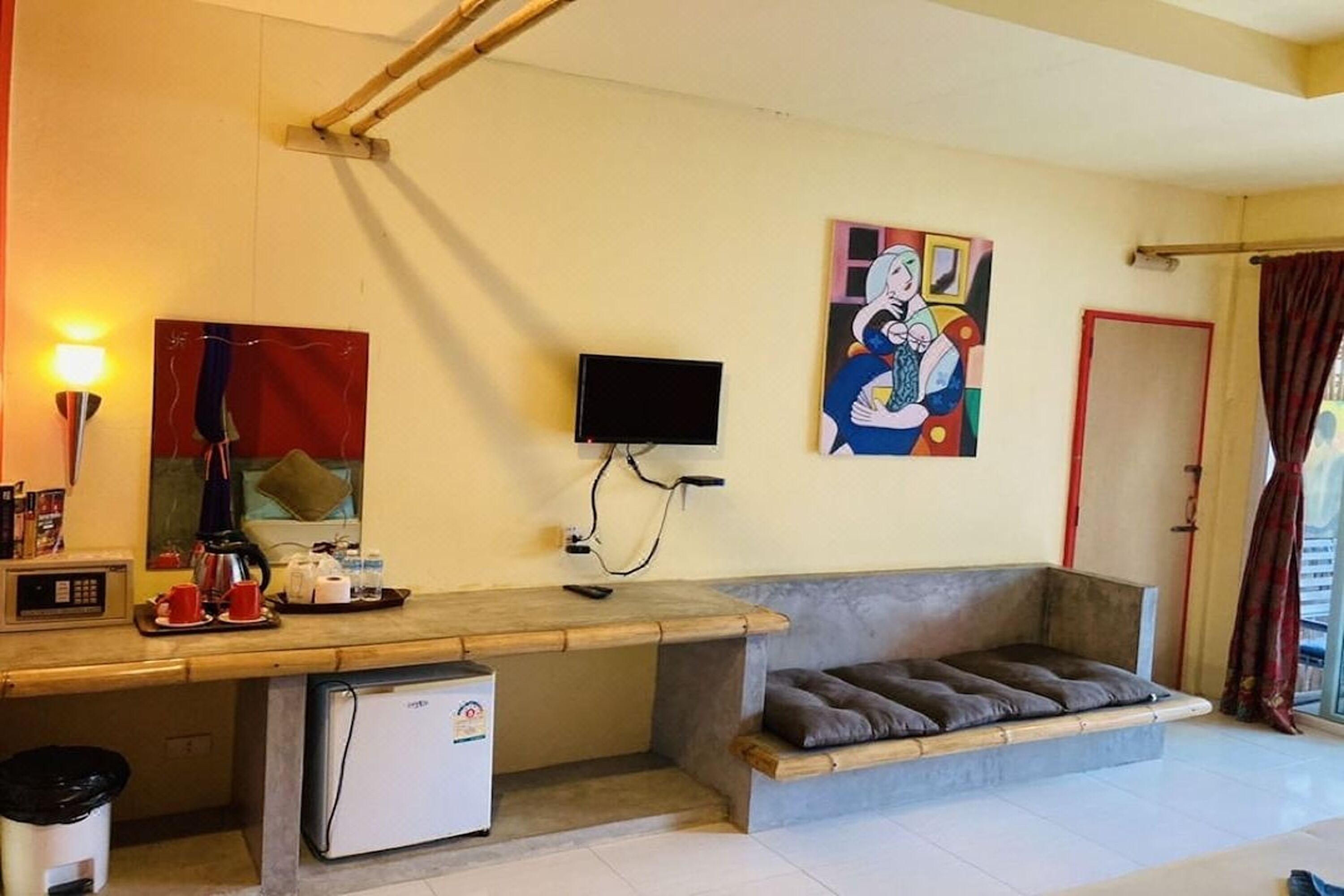Un espace de vie compact comprenant un coin cuisine, un téléviseur à écran plat fixé au mur, un canapé avec des coussins et une fenêtre avec des rideaux.