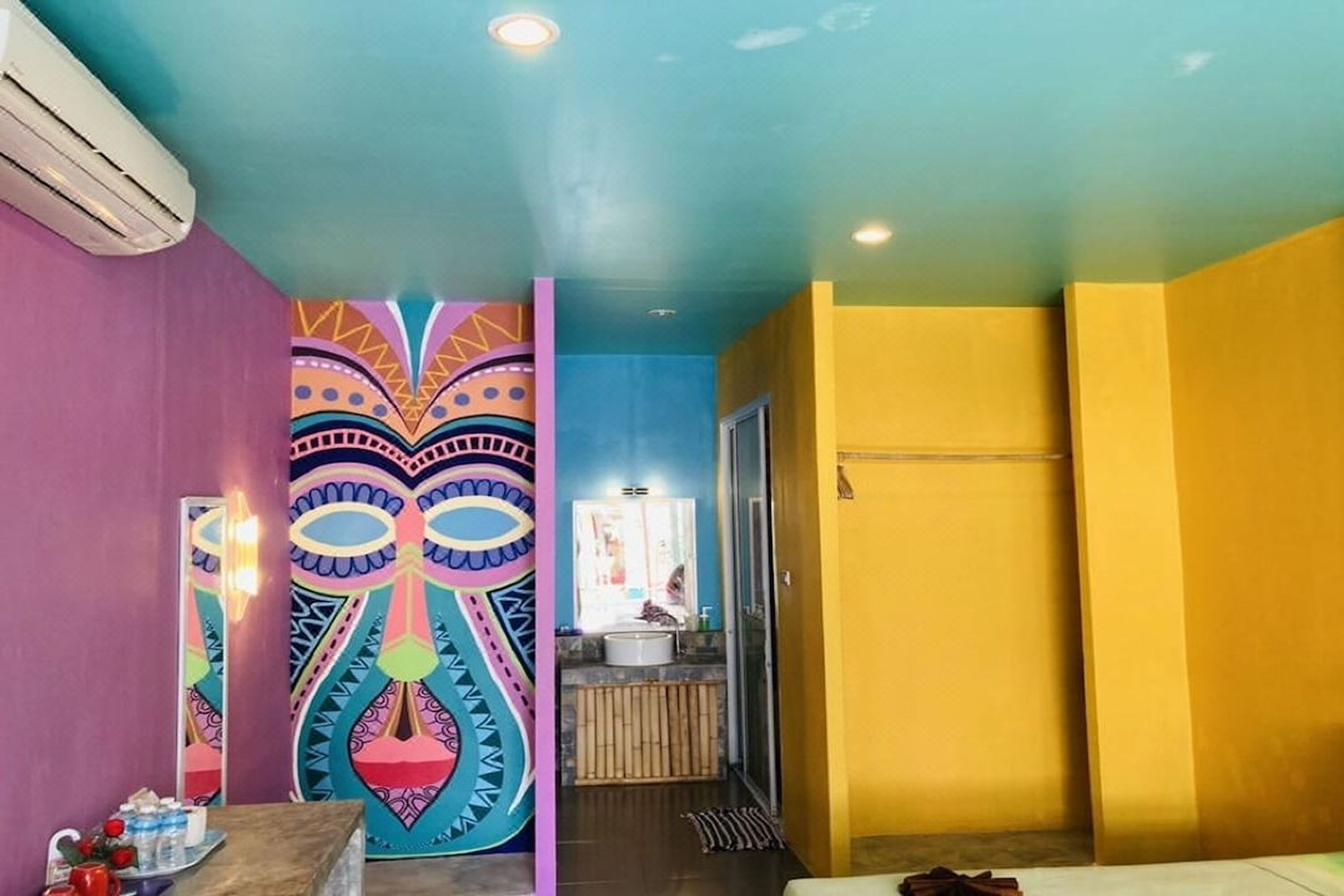 A room with a colorful mural, a sink, and a wooden bench.