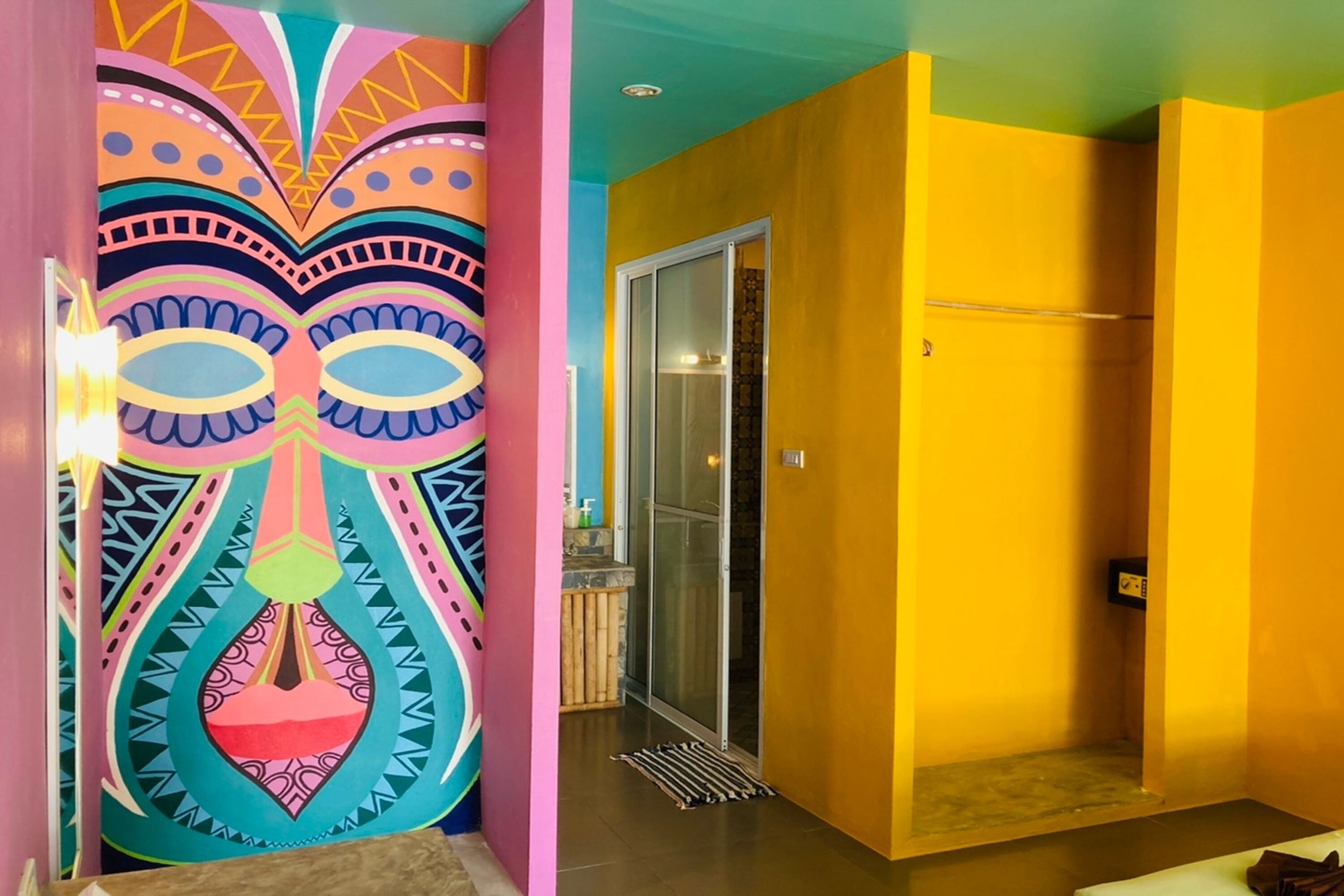 A room with a colorful mural on one wall, a sliding glass door leading to a balcony, and a yellow wall on the other side.