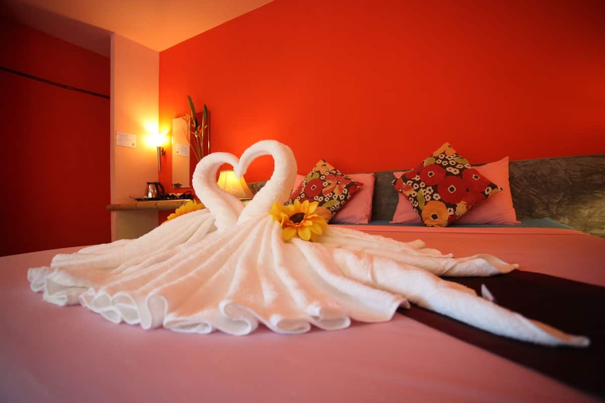 A bed with a towel arranged in the shape of a swan, a lamp, and decorative pillows.