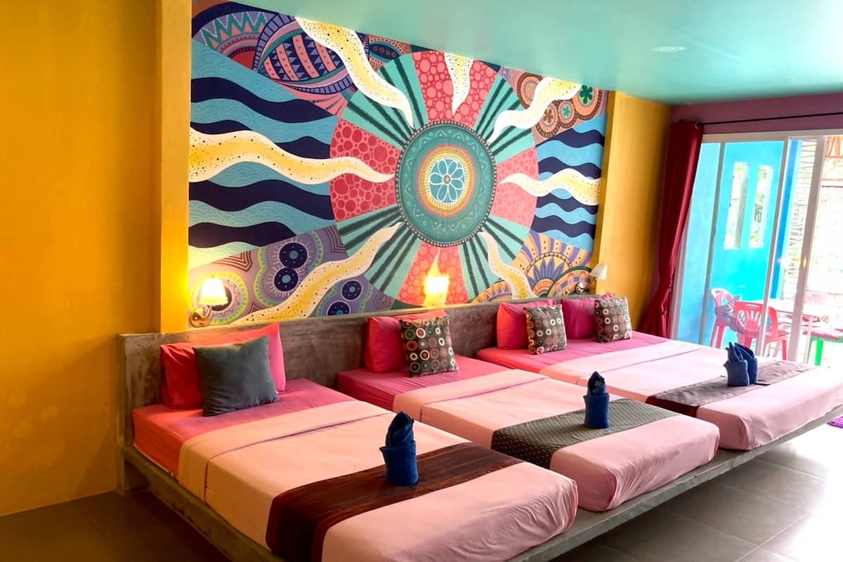 A room with three beds, colorful wall art, and a view of the outside.