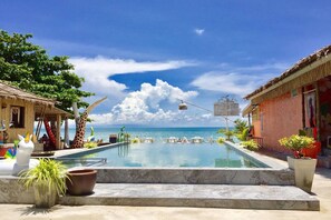A swimming pool with lounge chairs, a giraffe statue, and a view of the ocean. - Chaba Bungalows (Ko Lanta)