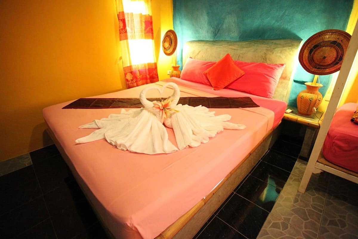 A hotel room with a bed, pink bedding, a heart-shaped towel arrangement, and a decorative wall.