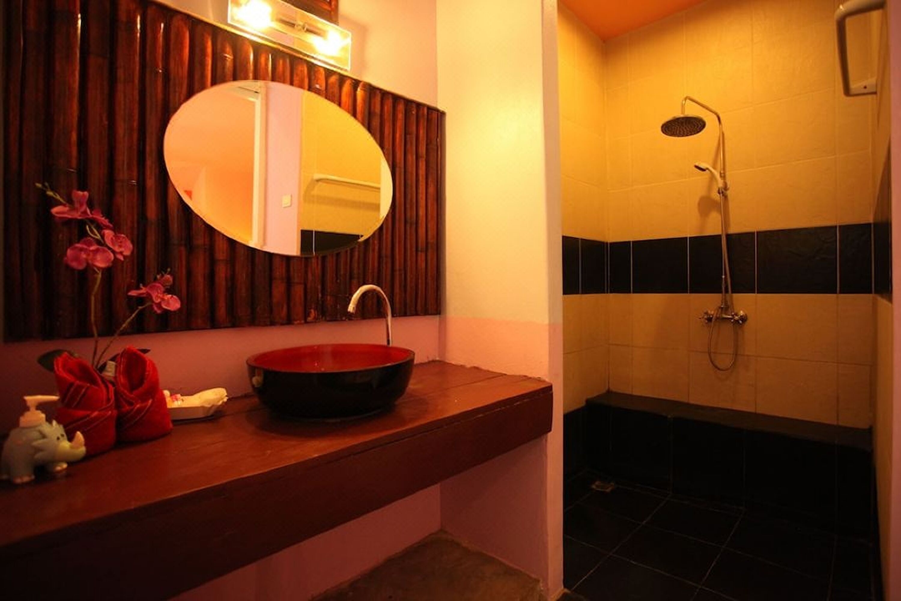 Une salle de bain avec un meuble-lavabo en bois, un miroir rond, un lavabo rouge et un espace douche.