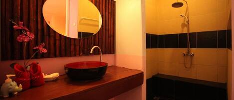 Une salle de bain avec un meuble-lavabo en bois, un miroir rond, un lavabo rouge et un espace douche.