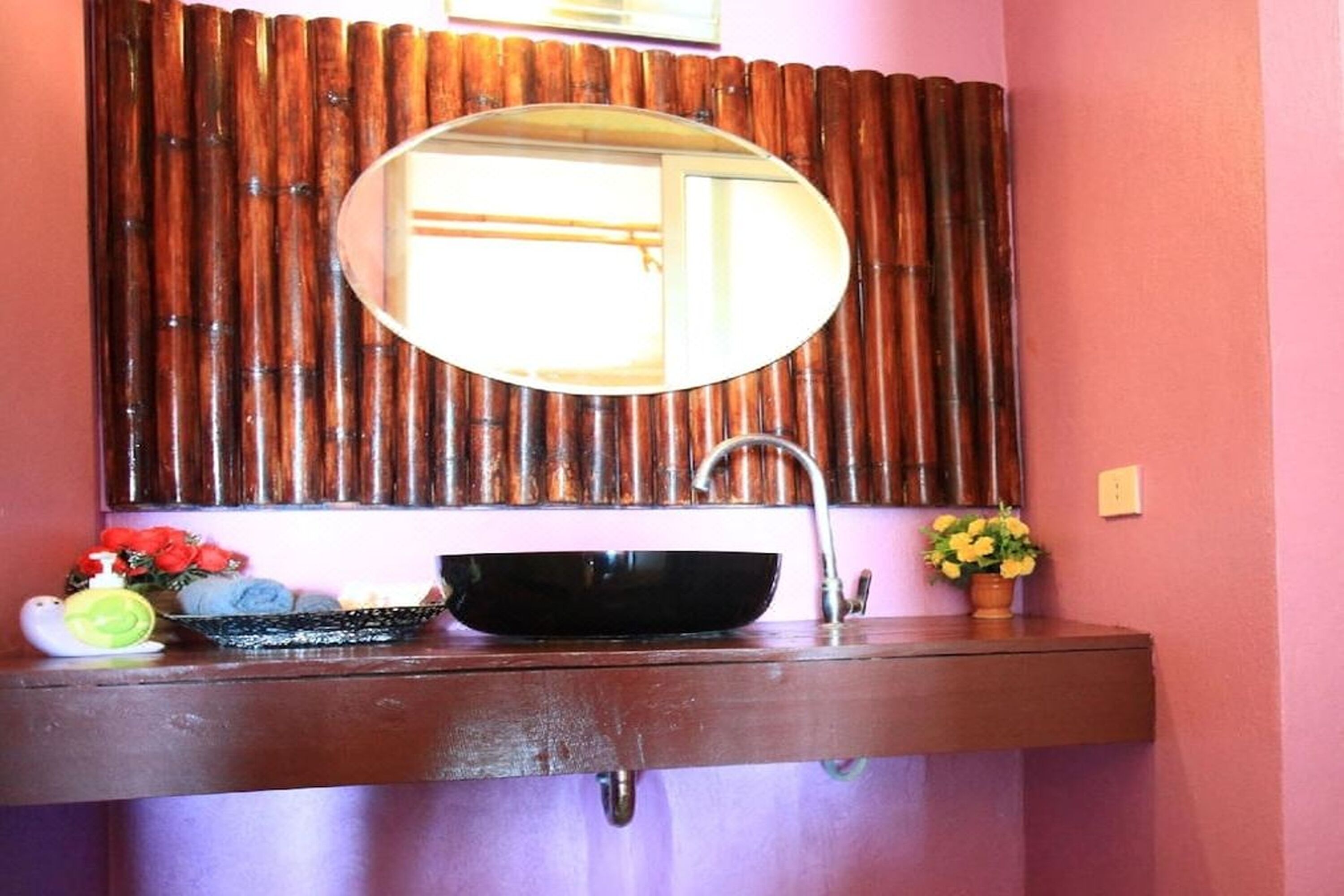 Un baño con un espejo redondo, un lavamanos negro y un panel de pared de bambú.