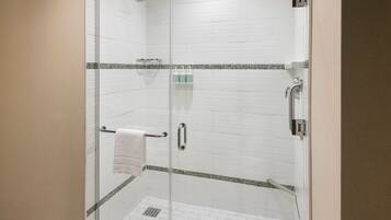 A glass-enclosed shower with white tiles, a towel rack, and a small shelf with toiletries.