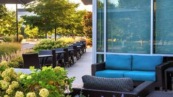 Een terras met rieten meubels en een blauwe bank, omgeven door groen en bomen.