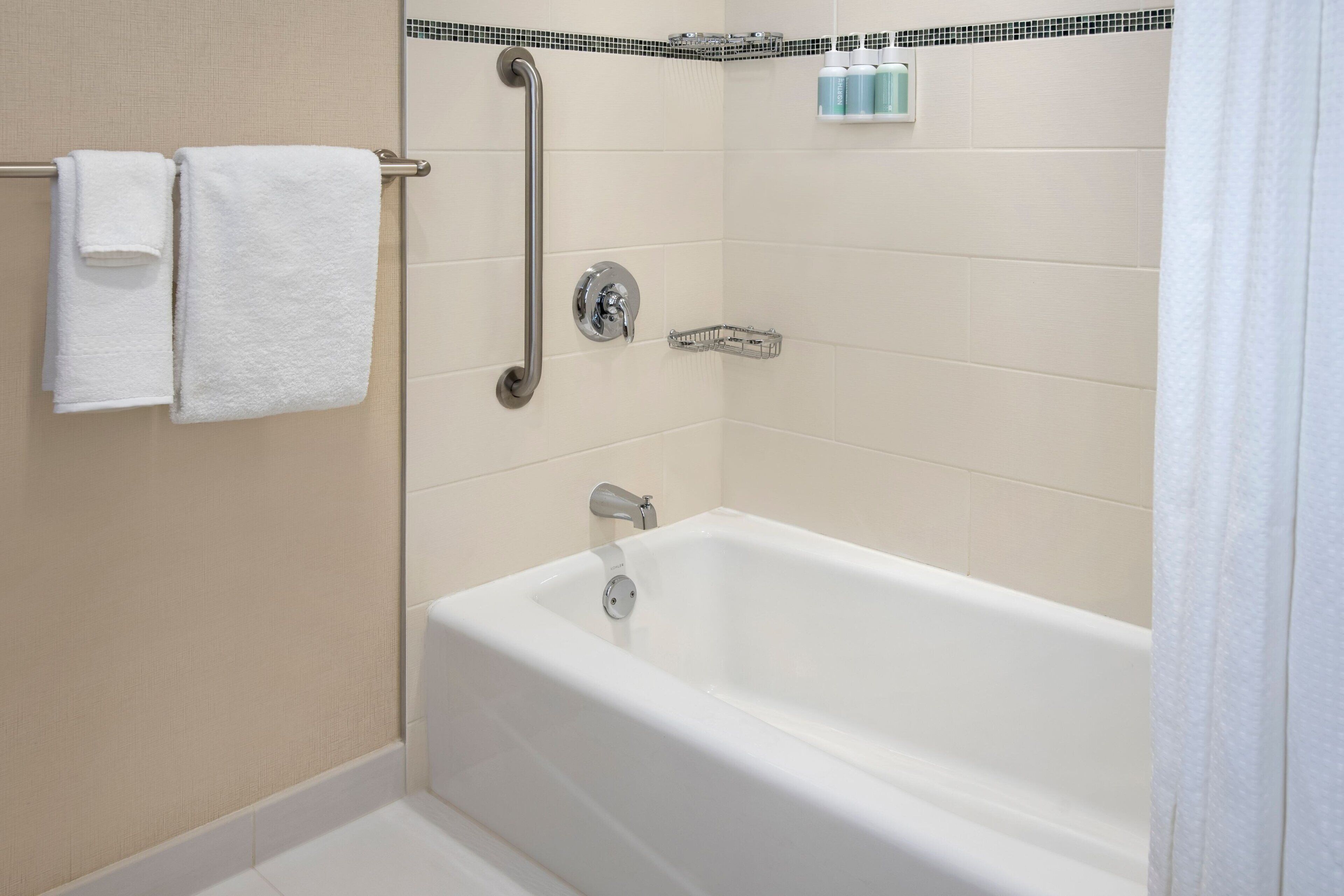 A modern bathroom with a white bathtub, a grab bar, and a towel rack.