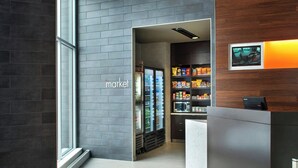 A modern interior with a reception desk, a refrigerator stocked with beverages, and shelves with snacks. - Courtyard Philadelphia South at The Navy Yard (Philadelphia)