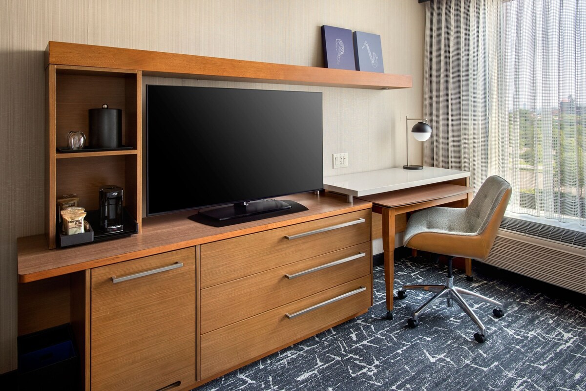 A hotel room with a wooden desk, a flat-screen TV, a coffee maker, and a chair.