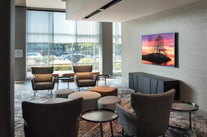 A modern lounge area with comfortable seating, a large window with a view of parked cars, and a wall-mounted TV.