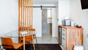 A compact living space with a glass dining table, two chairs, a kitchenette with a microwave, and a small refrigerator. - Merivale Court Motel (Christchurch)