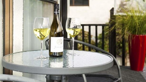 A round metal table with two wine glasses and a bottle of wine on a balcony. - Merivale Court Motel (Christchurch)