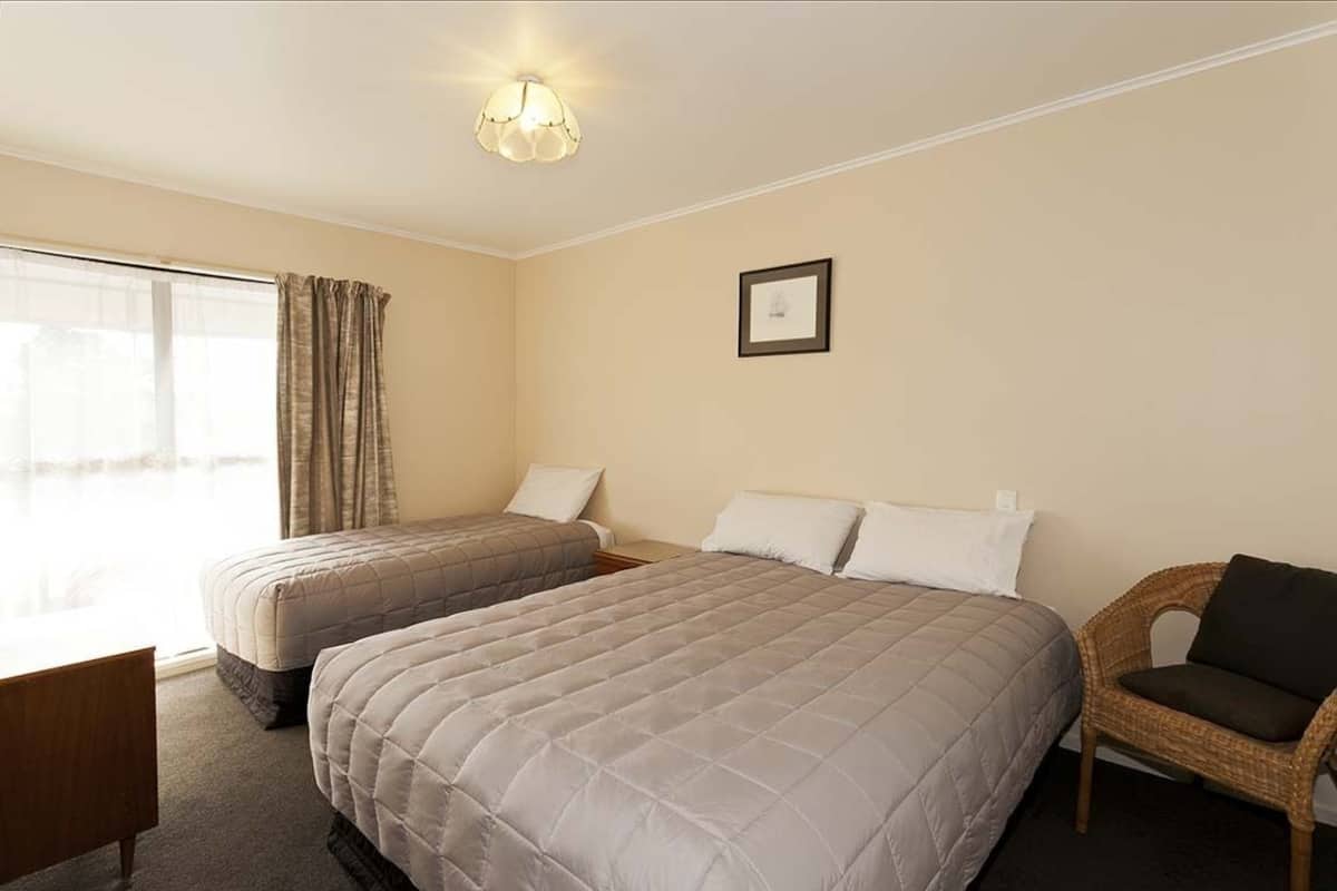 A hotel room with two beds, a chair, a desk, and a window with curtains.