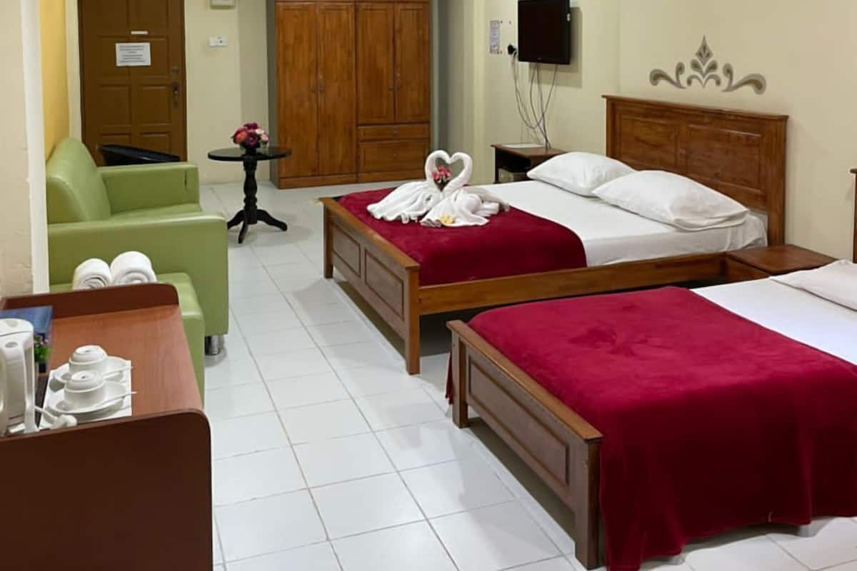Ein Hotelzimmer mit zwei Betten, einem grünen Sessel, einem Holzschrank, einem Fernseher und einem kleinen Tisch mit einer Vase.