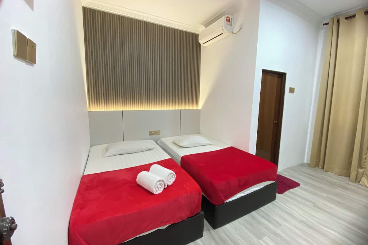 Ein Hotelzimmer mit zwei Betten, einer Decken-Klimaanlage, einer Wandleuchte und einer Tür mit Vorhängen.