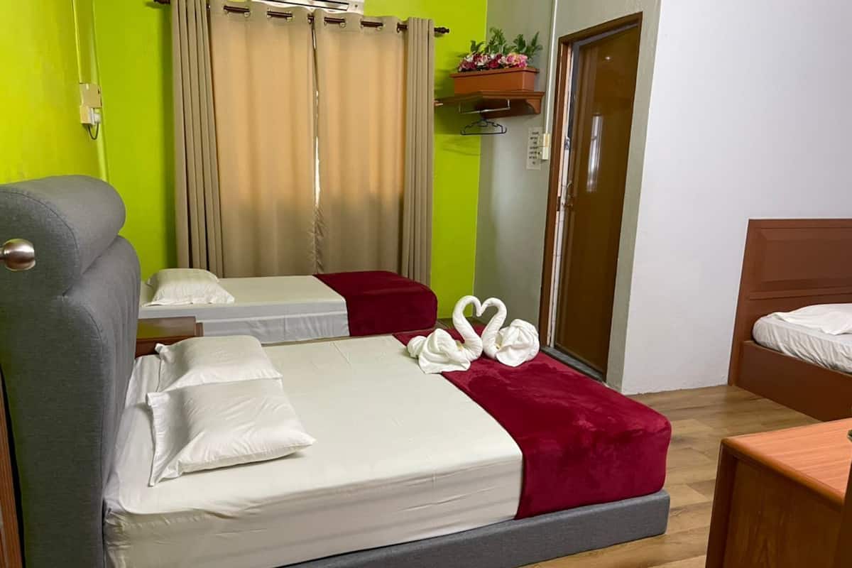 Ein Hotelzimmer mit zwei Betten, einem grauen Sofa, einem roten Zierkissen und einem Nachttisch aus Holz.
