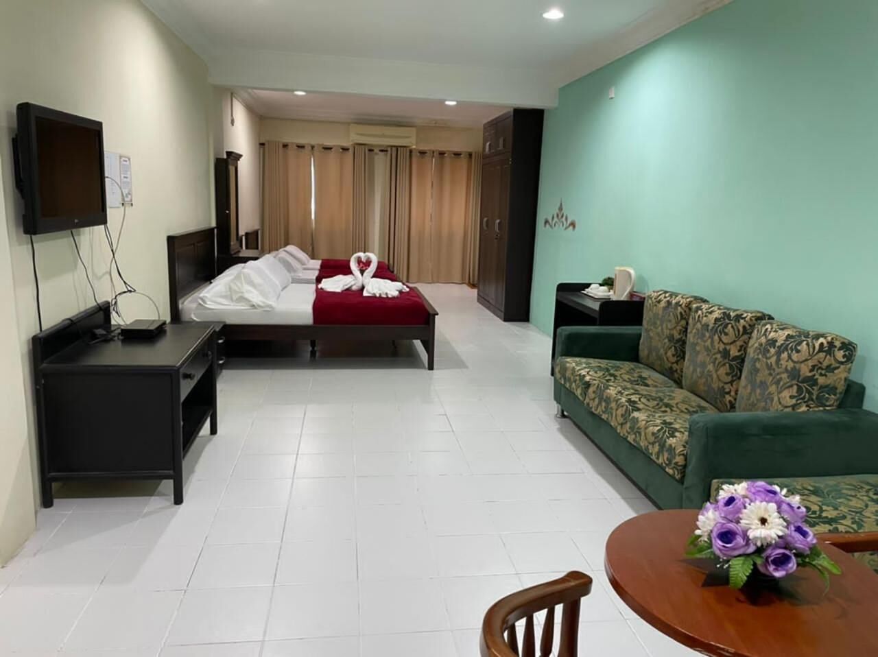 A hotel room with a bed, a sofa, a TV, a desk, and a small table with flowers.