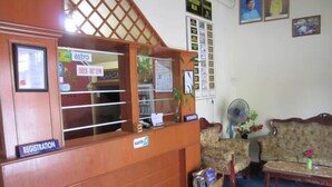 A reception area with a registration desk, a waiting area with a sofa and a fan, and a wall with various posters and a clock. - Samudera Hotel (Kuala Besut)