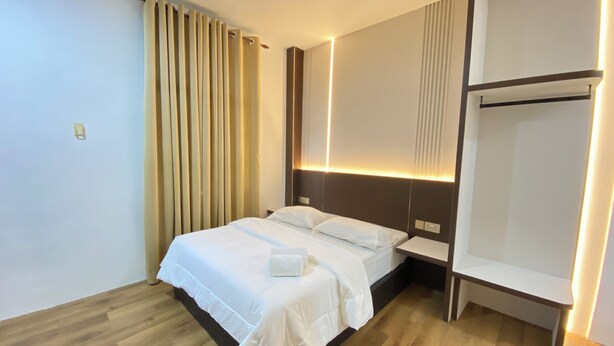 A modern hotel room with a wooden floor, a bed with white linens, a nightstand, and a wall-mounted shelf. - Samudera Hotel (Kuala Besut)