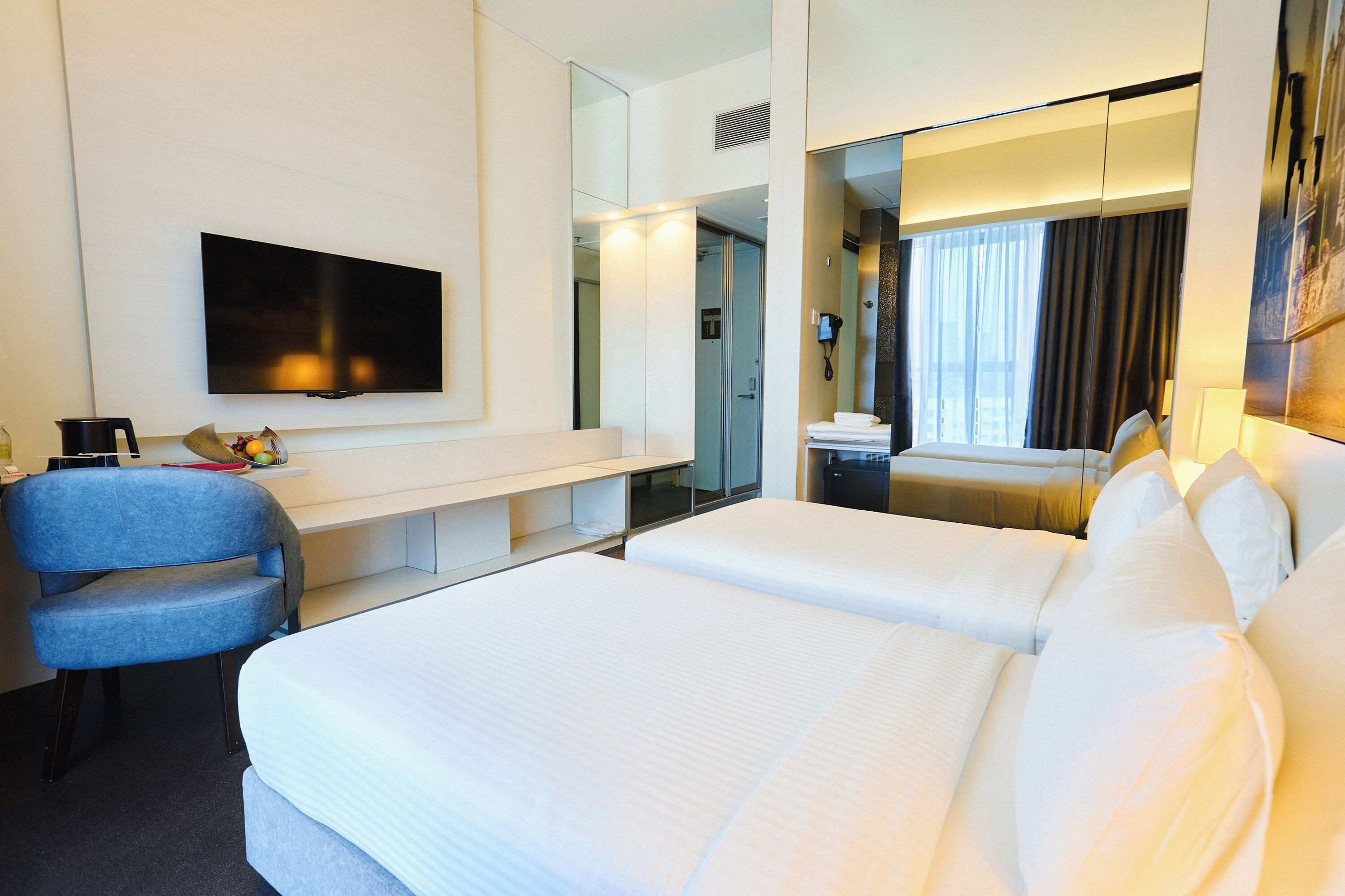 Habitación de hotel con una cama grande, un escritorio con silla, televisión y baño visible a través de una puerta de cristal.