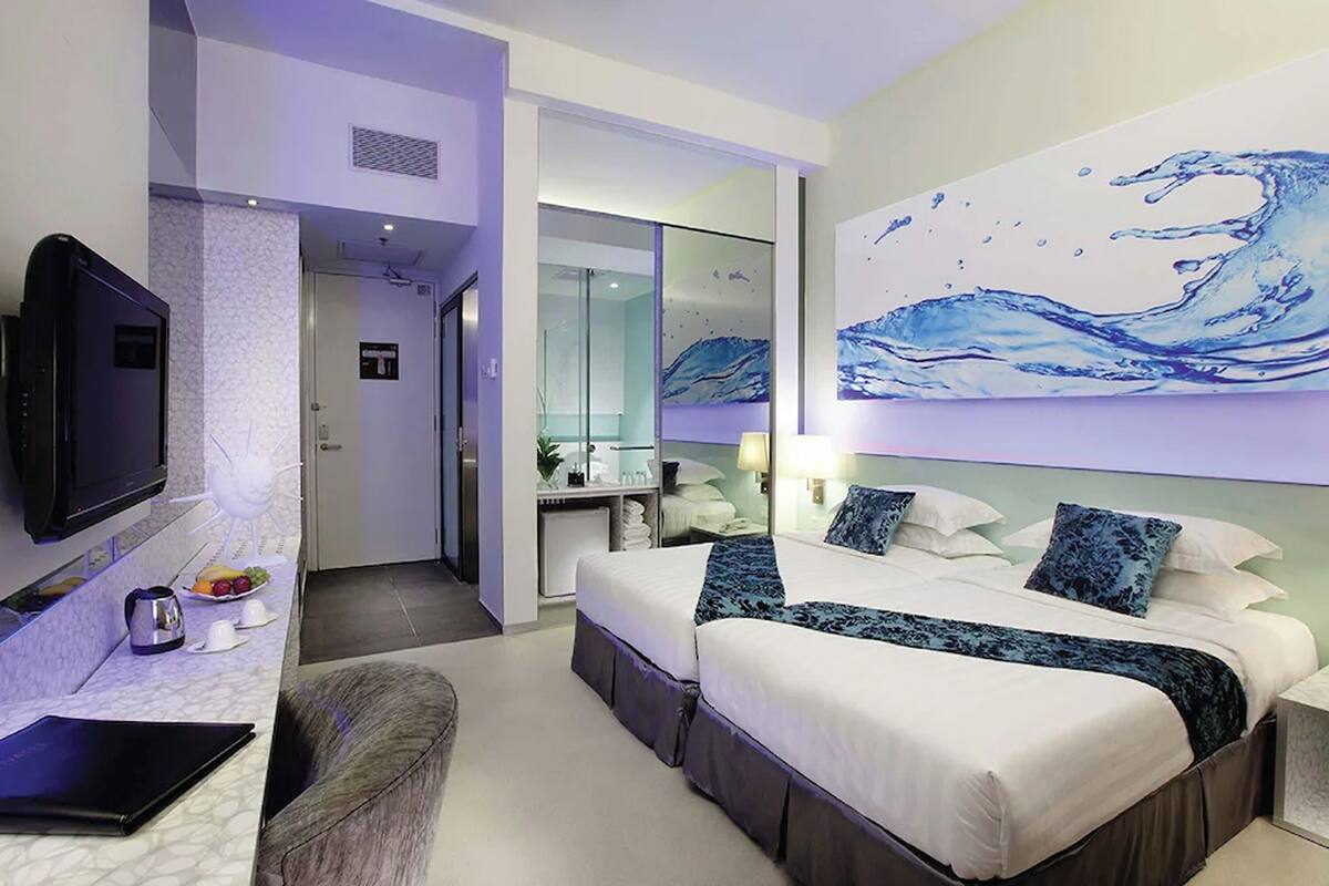 Ein modernes Hotelzimmer mit einem großen Bett, einem Schreibtisch mit einem Laptop, einem Flachbildfernseher und einem Wellenbild an der Wand.