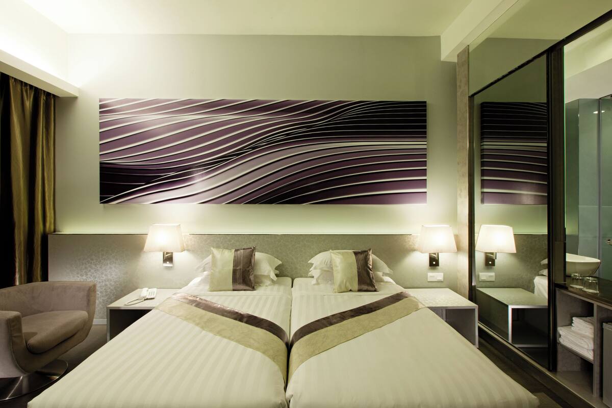 Ein Hotelzimmer mit zwei Betten, einem großen Spiegel, einem Sessel und einem Wandbild.