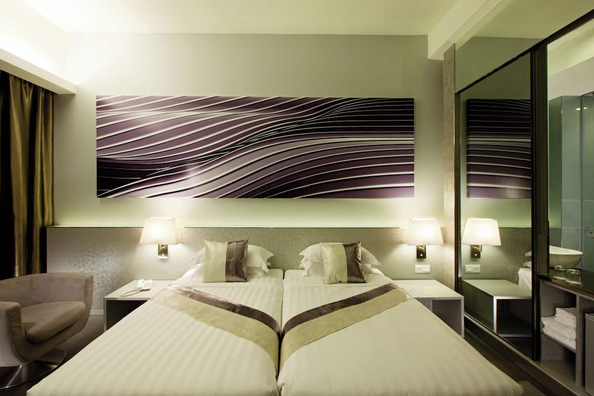 Ein Hotelzimmer mit zwei Betten, einem großen Spiegel, einem Sessel und einem Wandbild.