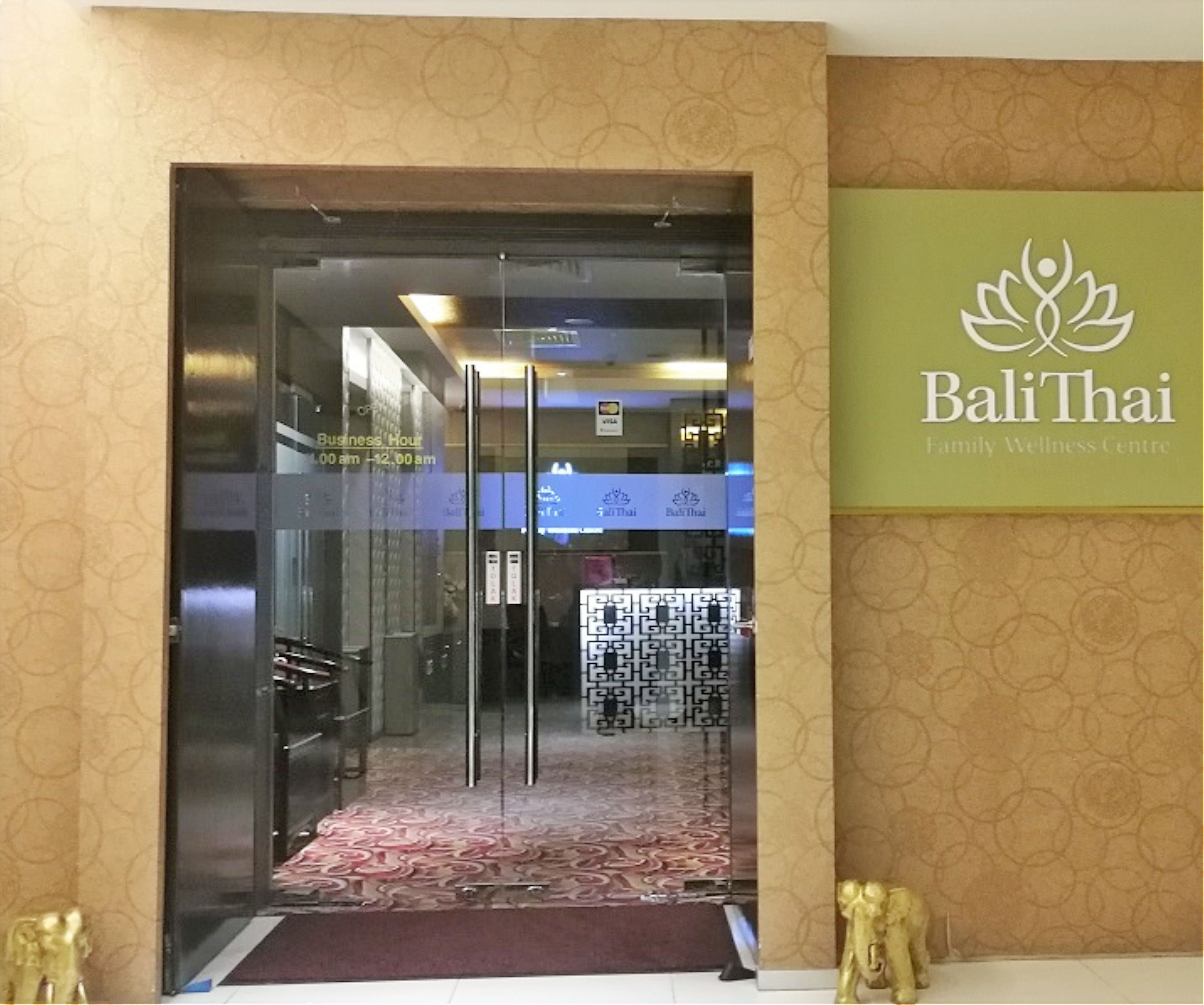 L’entrée du centre de bien-être Bali Thai Family, avec une porte en verre, un tapis à motifs et une enseigne au-dessus de la porte.