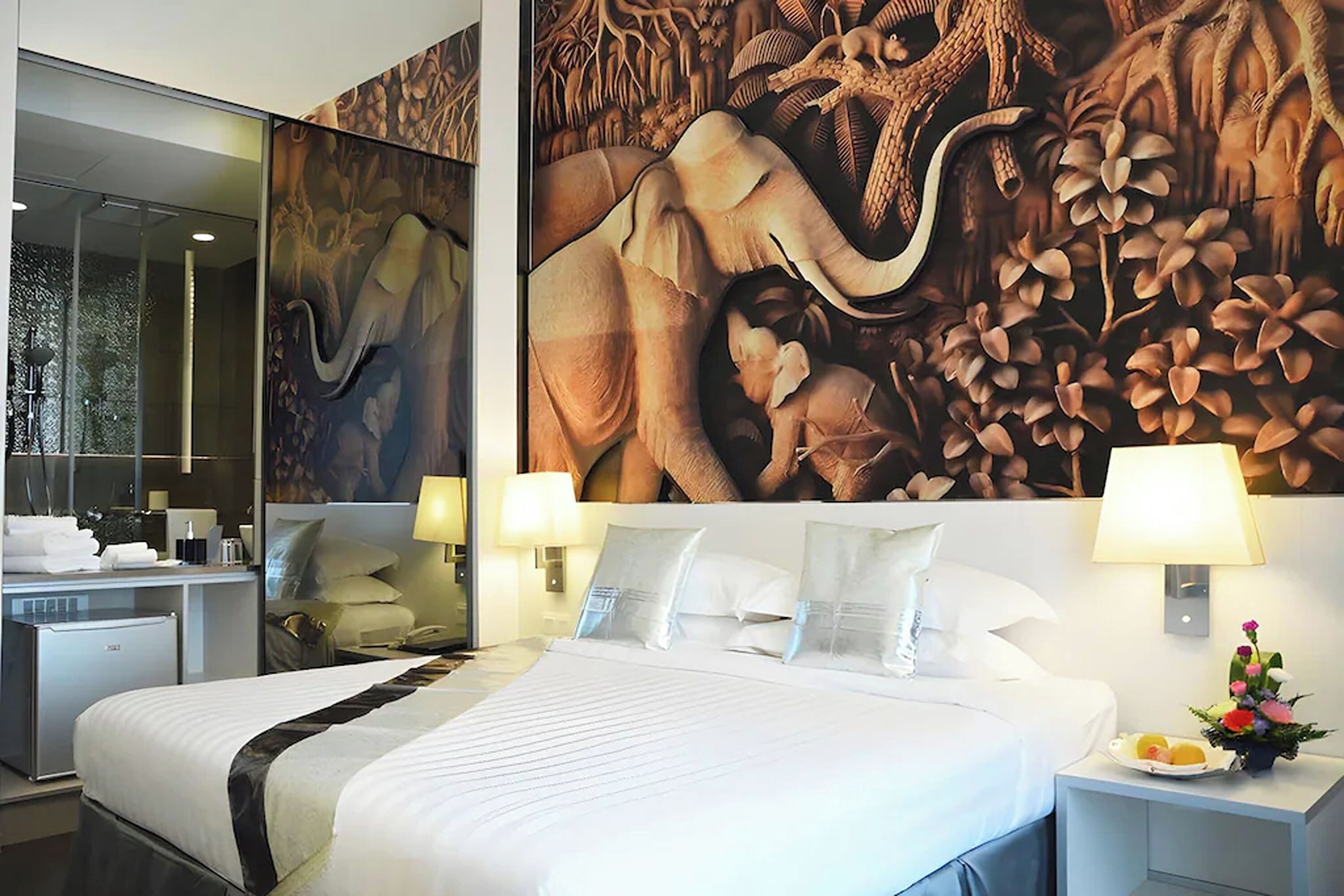 Une chambre d’hôtel avec un grand lit, deux tables de chevet, un miroir et une fresque murale.