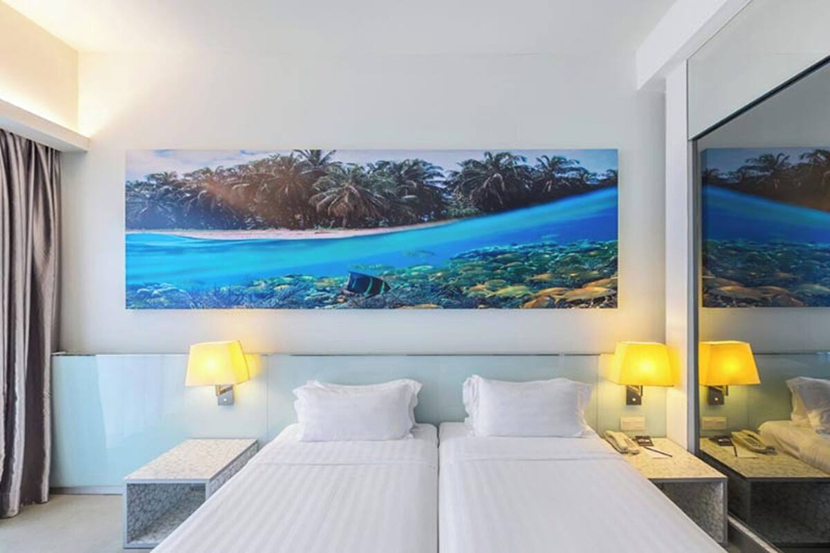 Ein Hotelzimmer mit zwei Betten, einem großen Gemälde einer Strandansicht und einem Spiegel an der Wand.