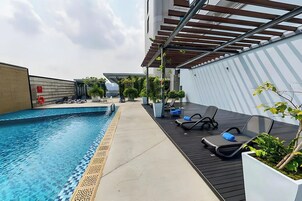 A rooftop pool area with a clear blue pool, lounge chairs, and potted plants.