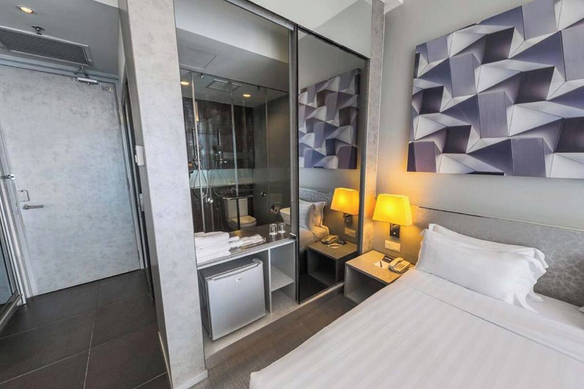 Ein modernes Hotelzimmer mit Bett, Nachttischlampen, Schreibtisch und einem durch eine Glastrennwand einsehbaren Badezimmer.