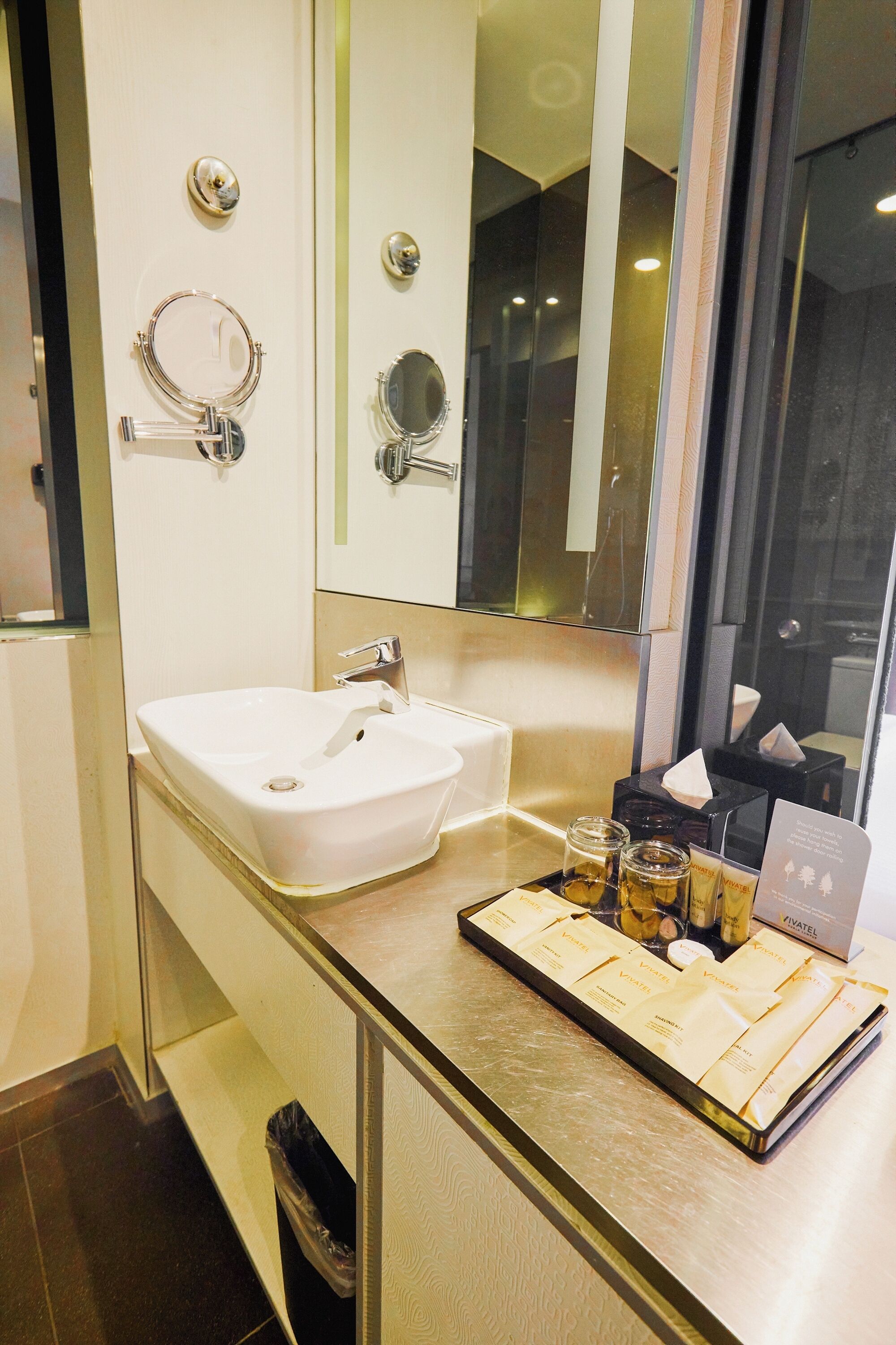 A modern bathroom with a white sink, two mirrors, and a tray with toiletries.