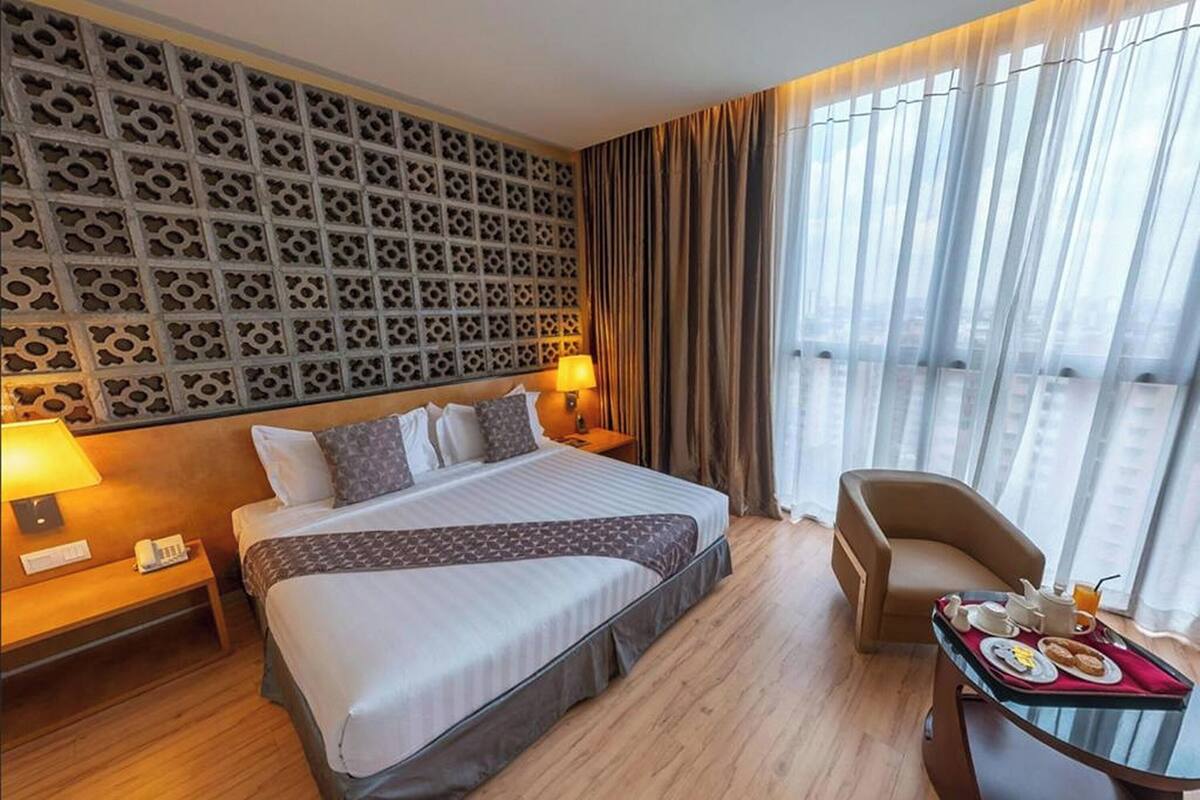Ein Hotelzimmer mit einem großen Bett, einem Nachttisch mit Lampe, einem Sessel und einem Frühstückstisch.