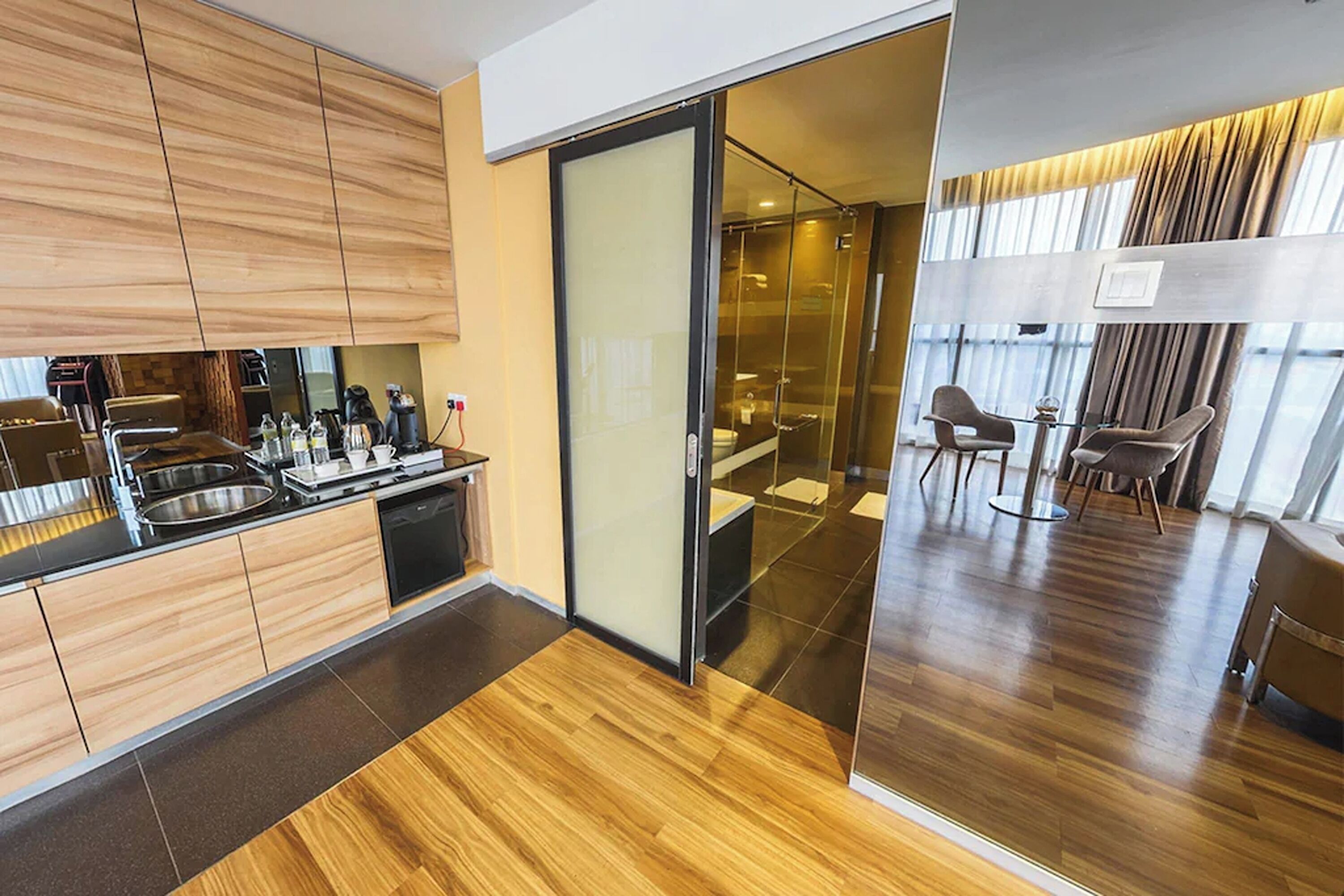 Cocina moderna con armarios de madera, lavavajillas y comedor separado por una pared de vidrio.