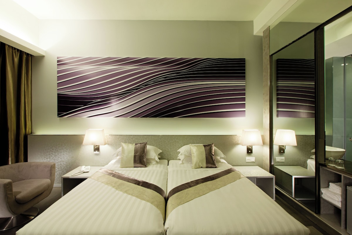 A hotel room with two beds, a chair, a large mirror, and a wall-mounted artwork.