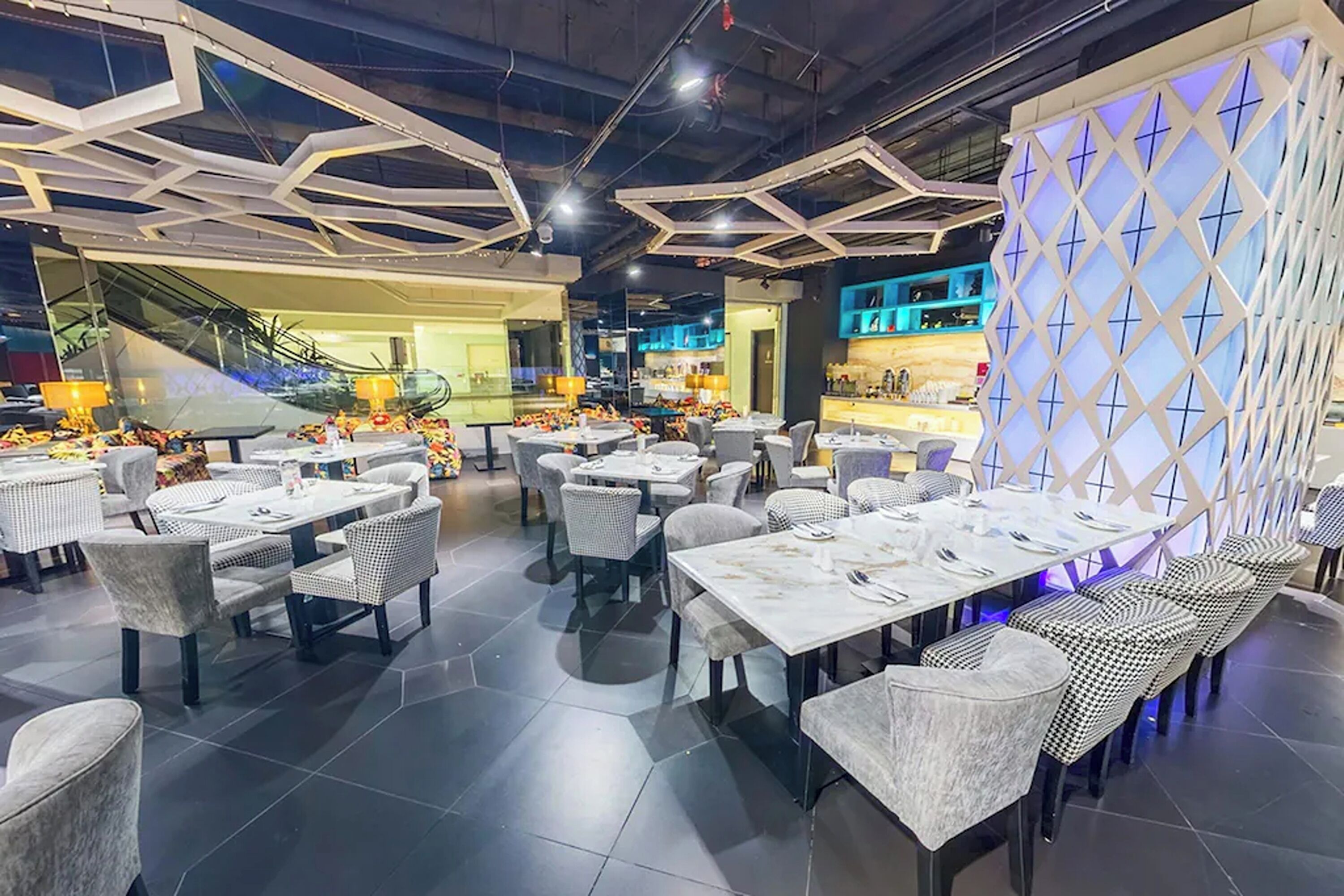 Un restaurante moderno con diseño de techo hexagonal, varias áreas de comedor y una escalera central.
