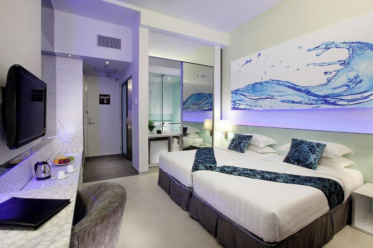 Ein modernes Hotelzimmer mit einem großen Bett, einem Fernseher, einem Schreibtisch mit einem Laptop und einem durch eine Glastür einsehbaren Badezimmer.