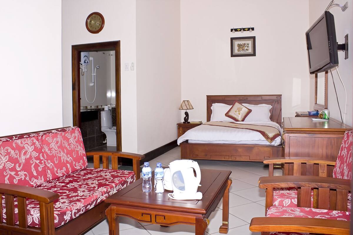 A hotel room with a bed, a sofa, a coffee table, a TV, and a bathroom visible through an open door.