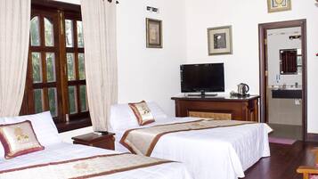 A hotel room with two beds, a television, a desk with a kettle, and a bathroom visible through an open door.