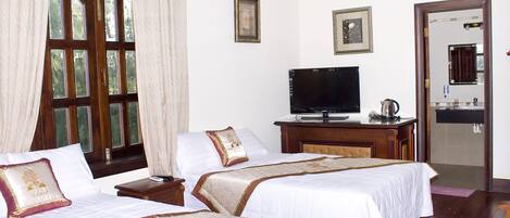 Habitación de hotel con dos camas, televisor, escritorio con hervidor y baño visible a través de una puerta abierta.