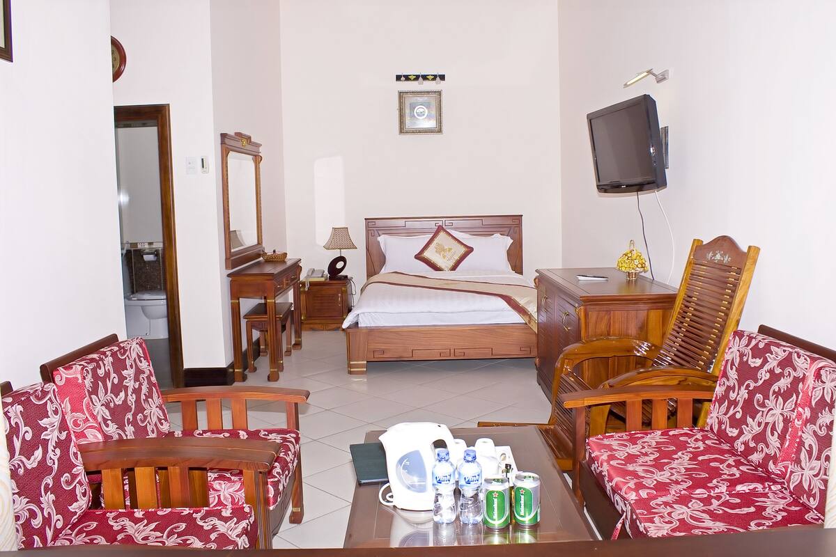A hotel room with a bed, a TV, a desk, a chair, and a table with drinks.