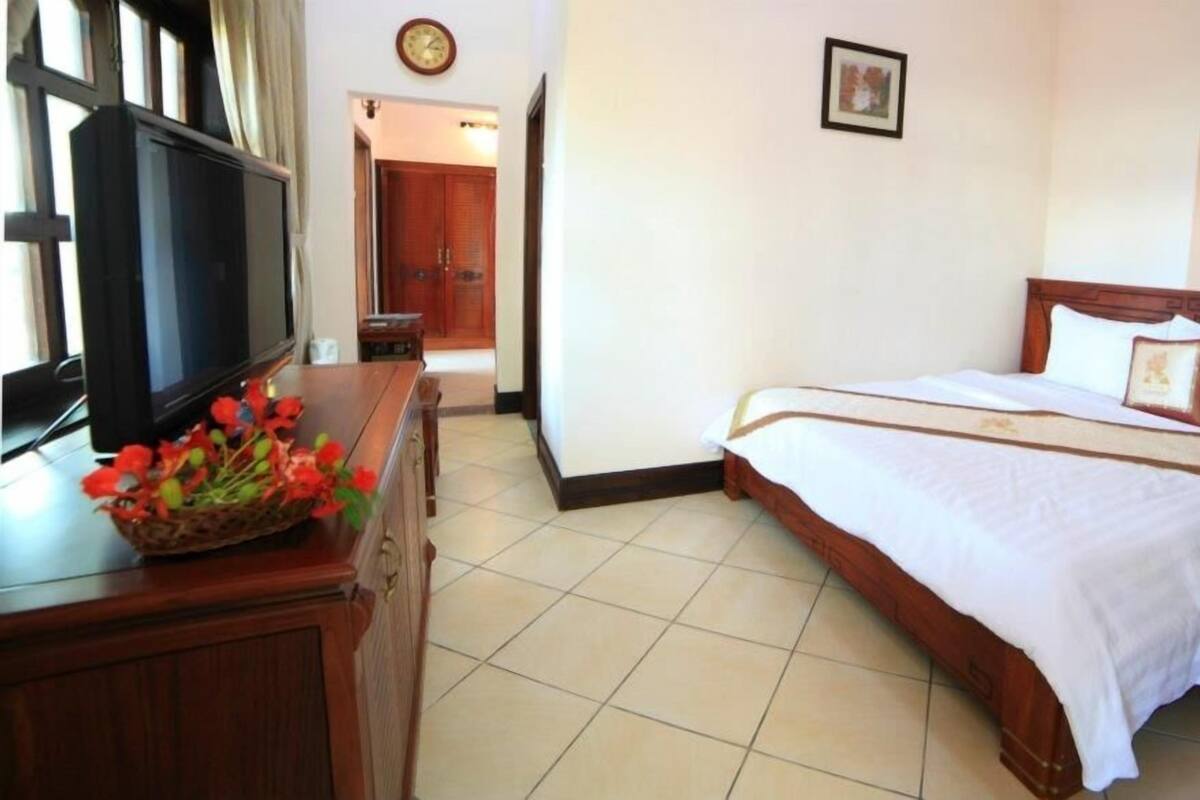 A hotel room with a bed, a TV, a wooden dresser, and a door leading to another room.