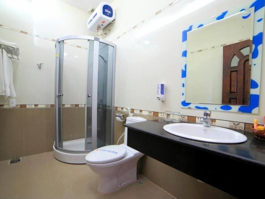 Un baño con ducha de vidrio, un inodoro blanco, un lavabo con espejo y un perchero para toallas.