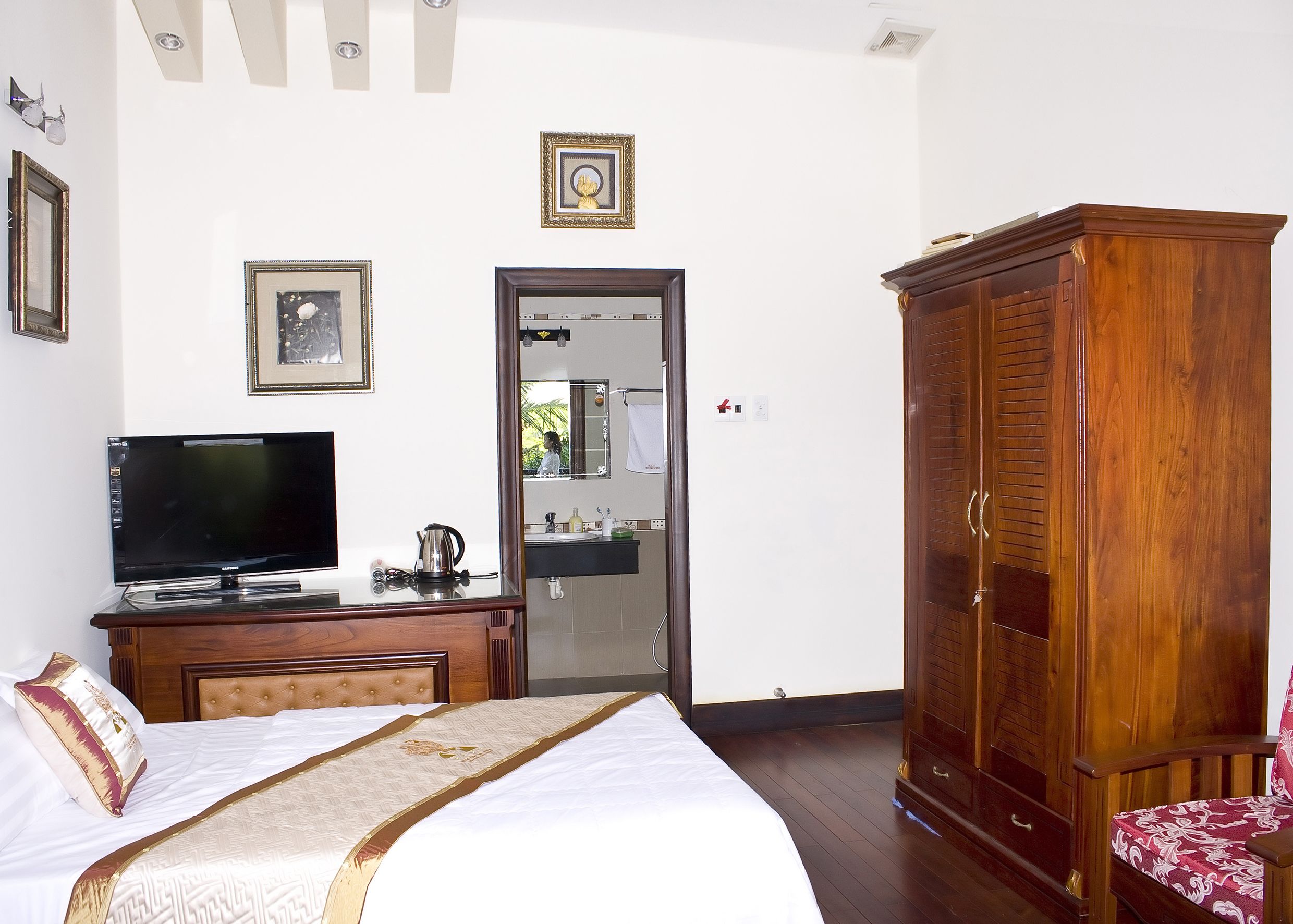 A hotel room with a bed, a television, a wooden wardrobe, and a mirror.