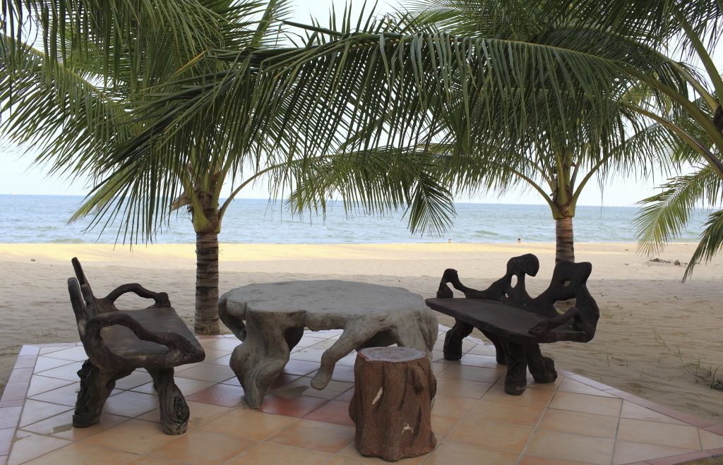 A beachside seating area with a round table and two chairs, surrounded by palm trees and a view of the sea.